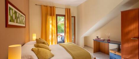 A bedroom with a bed, bedside lamp, wooden wardrobe, and a desk with a chair.