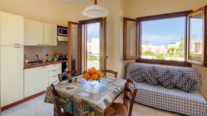 Eine kompakte Küche mit Essbereich, ein Sofa mit gemusterten Kissen und Blick durch große Fenster.