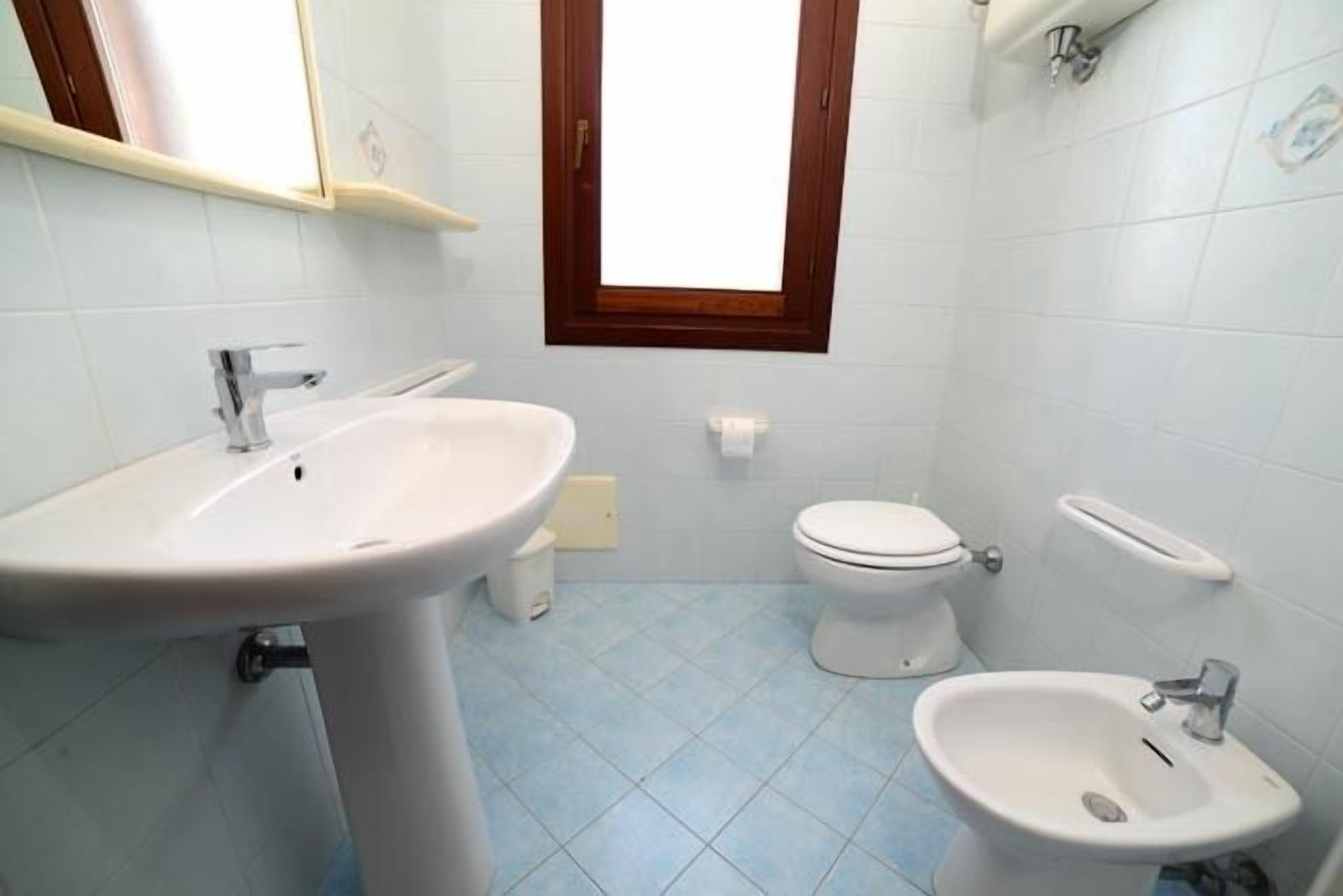 A bathroom with a sink, toilet, bidet, and a window above the toilet.