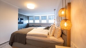 A bedroom with a bed, bedside lamps, and a view of a kitchen area. - Ratshotel (Haltern am See)