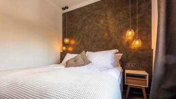 A neatly made bed with white bedding and two pillows, a bedside table with a lamp, and a textured wall behind the bed.