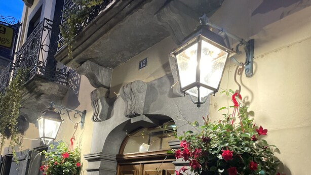 A hotel entrance with a wooden door, a sign reading "HOTEL du LIONDOR," and flower baskets on the wall.