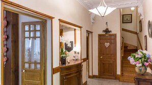 A hallway with wooden doors, a mirror, a vase with flowers, and a staircase.