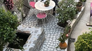 A stone-tiled patio with a round table and chairs, surrounded by potted plants and a stone wall.