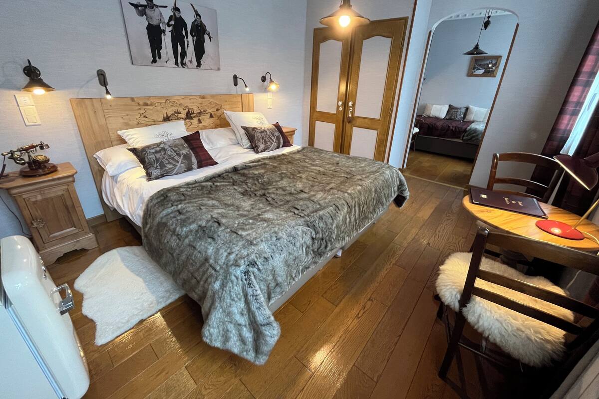 Un dormitorio con una cama grande, un cabecero de madera, un escritorio con silla, un espejo y un cuadro colgado en la pared.