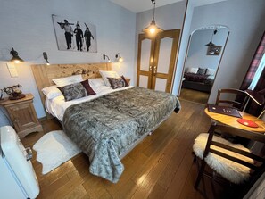 Un dormitorio con una cama grande, un cabecero de madera, un escritorio con silla, un espejo y un cuadro colgado en la pared.