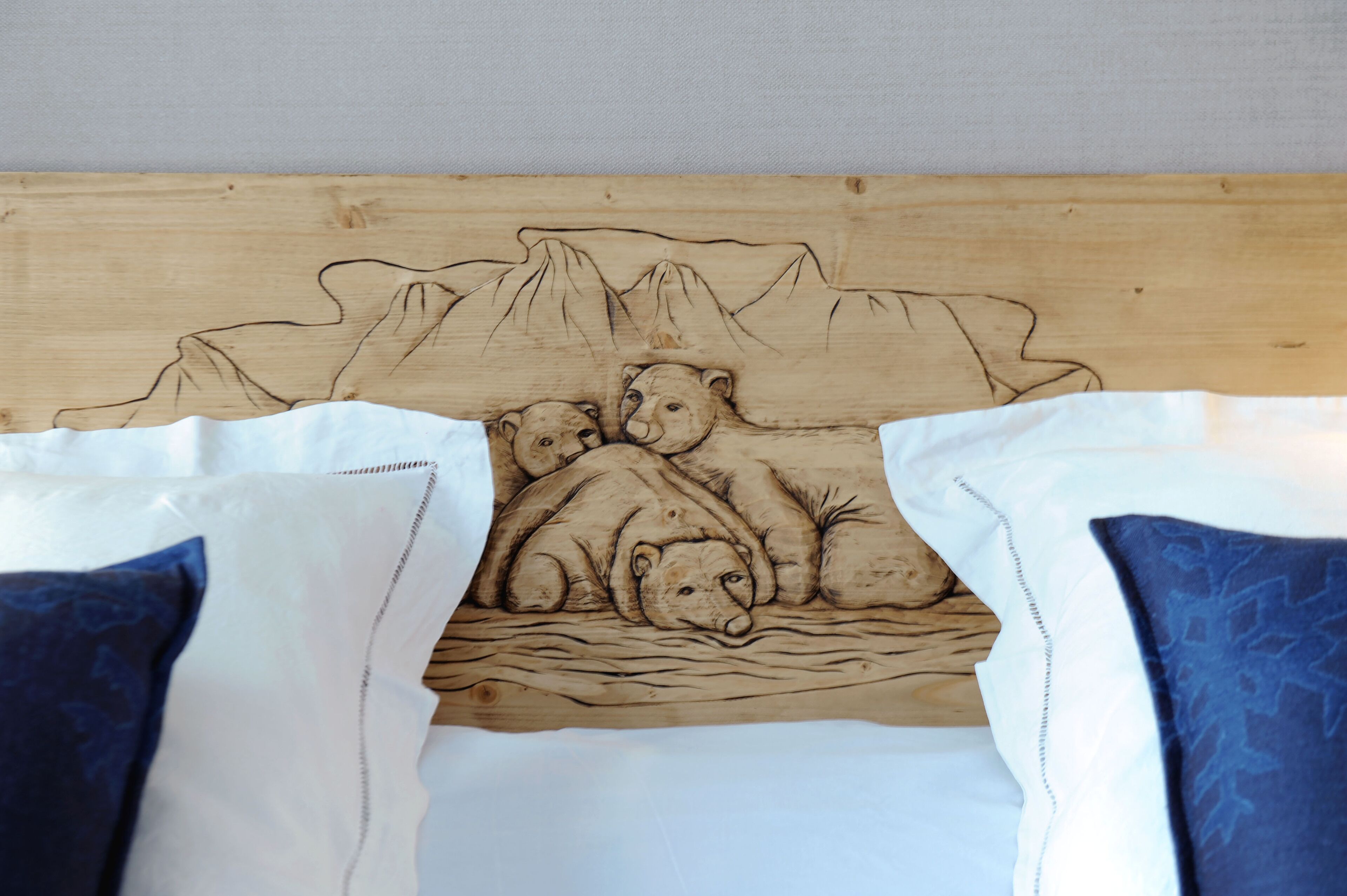 A bed with a carved wooden headboard depicting a family of bears by a lake, with white and blue pillows.
