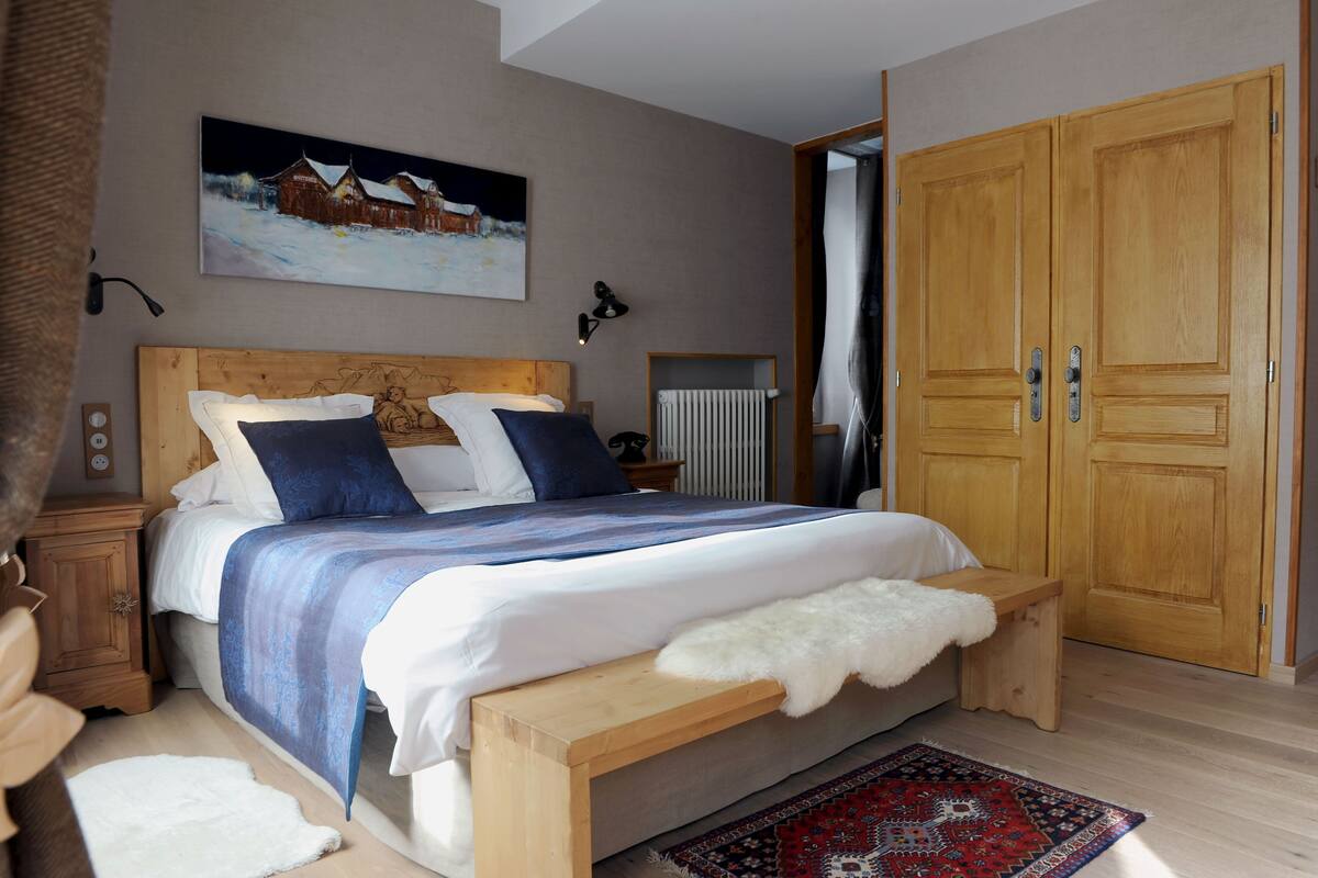Un dormitorio con una cama grande, cabecera de madera, mesitas de noche, una mesita auxiliar, un radiador y un armario.