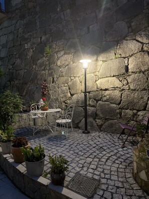 Un patio de piedra con una mesa y sillas, una farola y plantas en macetas.