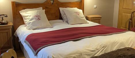 A bedroom with a wooden headboard, two bedside tables, a red throw blanket, a fluffy white pillow, and a framed alphabet poster on the wall.