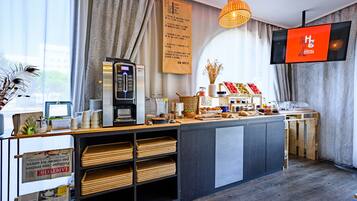 A modern hotel reception area with a coffee machine, a TV screen, and a menu board.