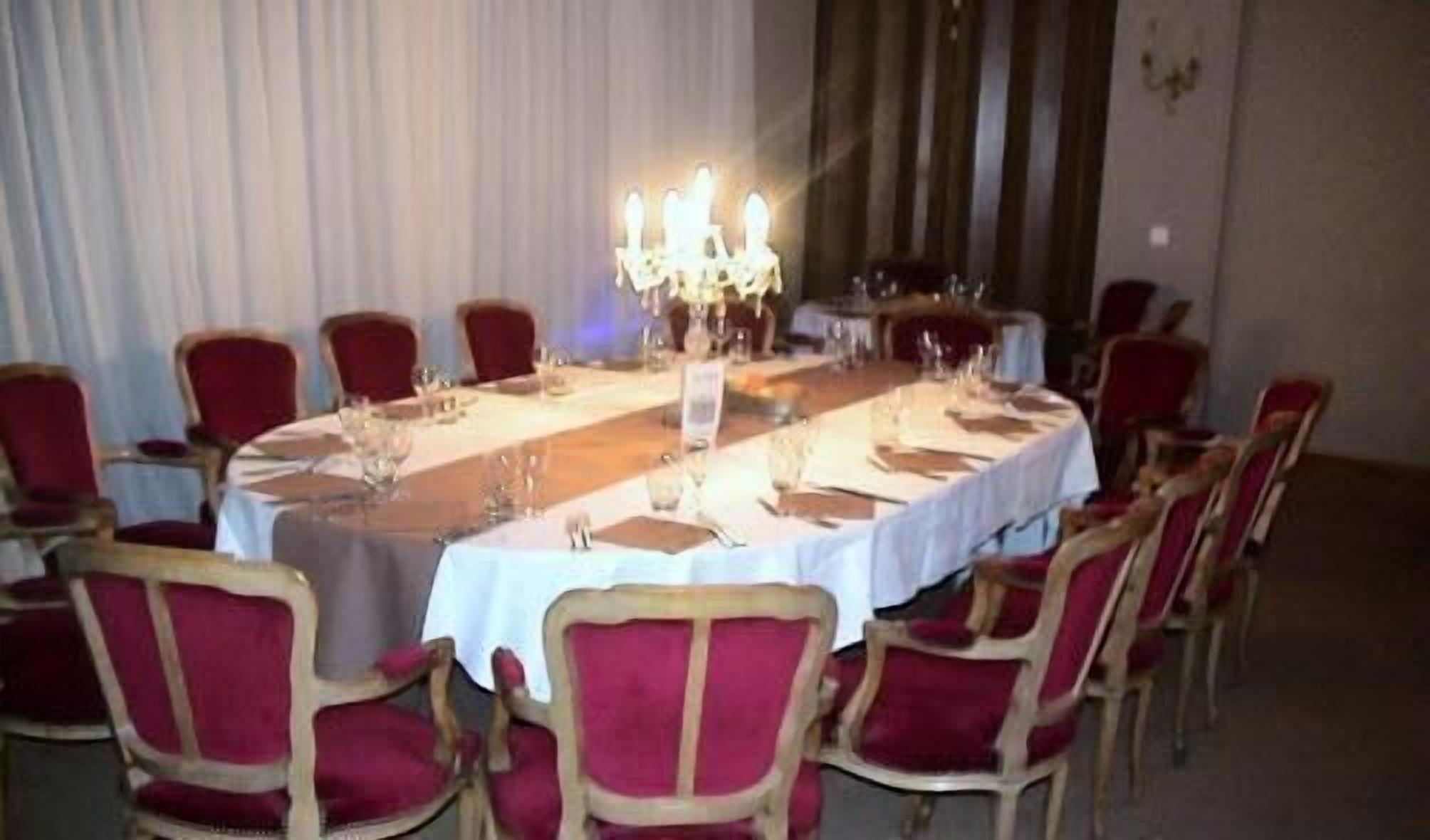 A round dining table with a white tablecloth, surrounded by red upholstered chairs.