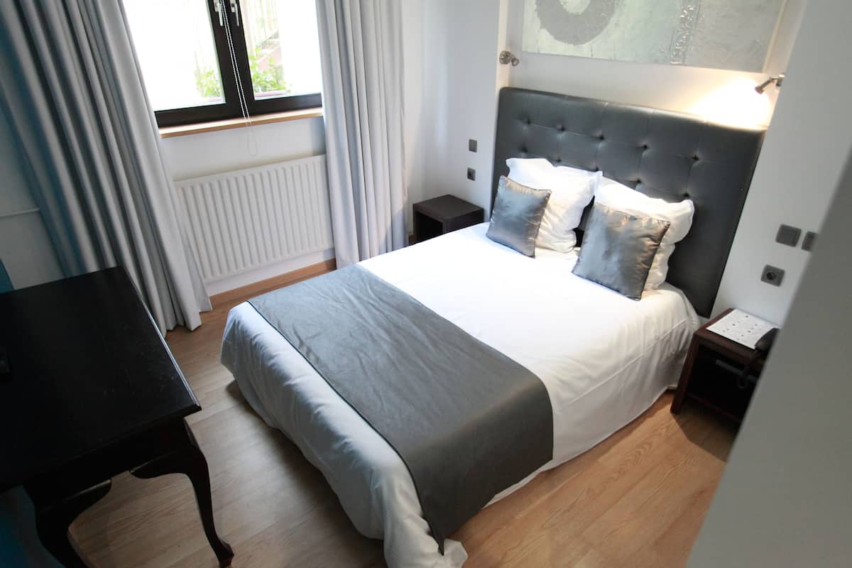A neatly arranged bedroom with a bed, bedside tables, a desk, and a window with curtains.