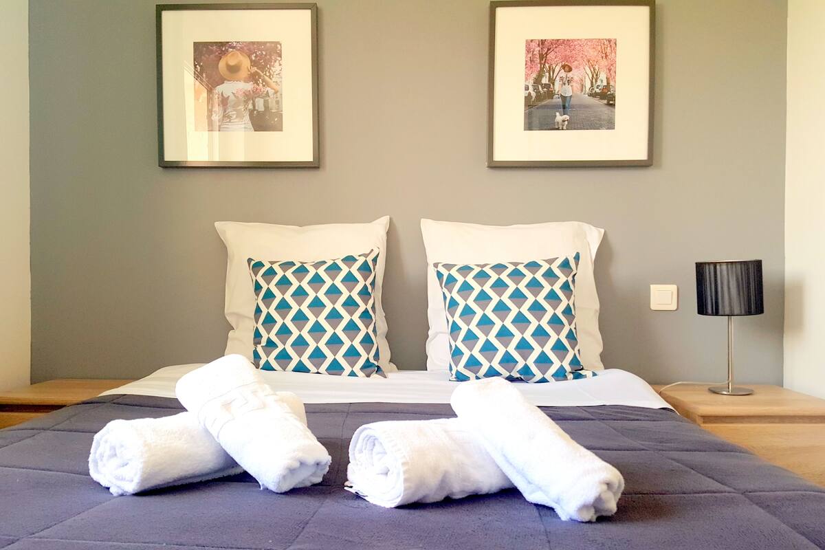 A neatly made bed with two pillows, a bedside table with a lamp, and two framed pictures on the wall.