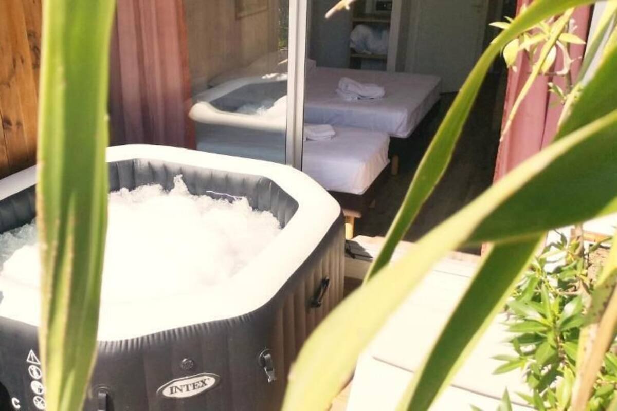 A hot tub with a wooden deck and a bed with white linens.