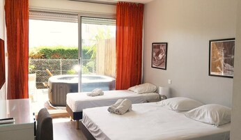 Habitación de hotel con dos camas, una bañera de hidromasaje y un balcón con cortinas naranjas.