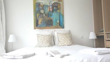 Una habitación de hotel con una cama, dos almohadas, un cuadro en la pared, una mesita de noche y una lámpara.