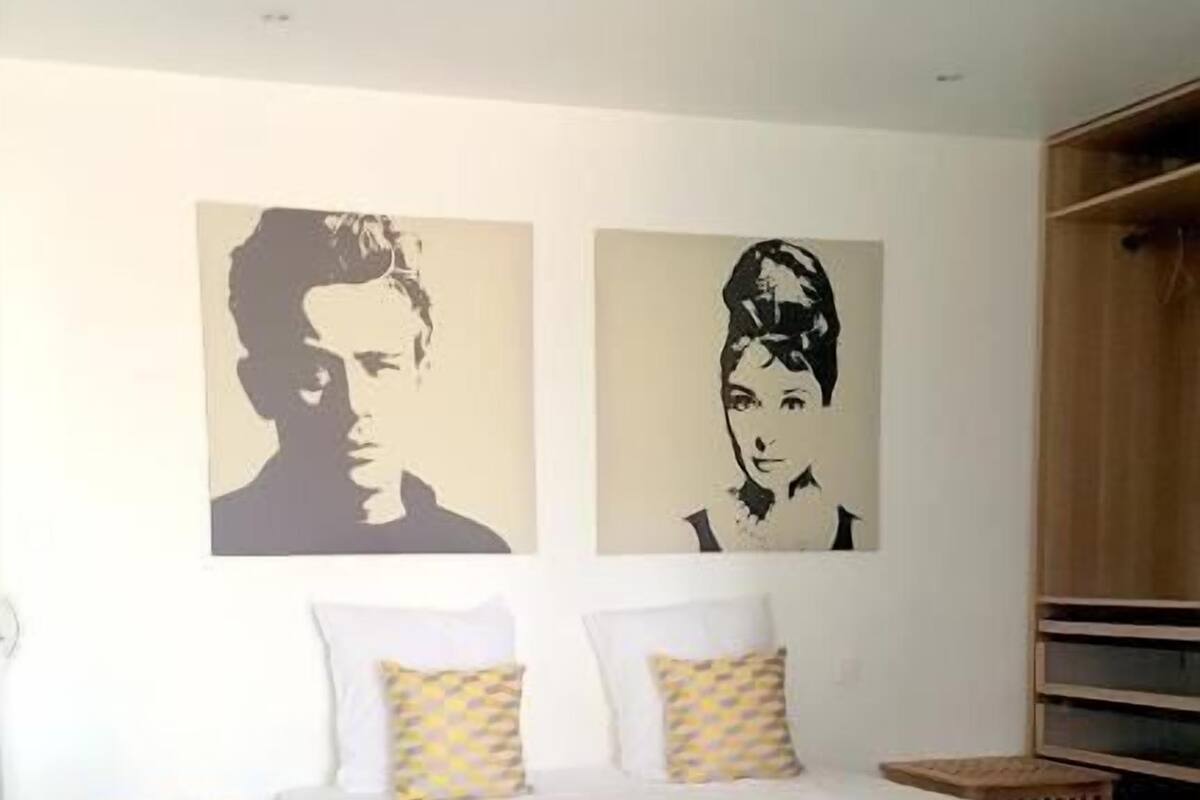 A bedroom with a bed, a chair, a wardrobe, and two wall art pieces.