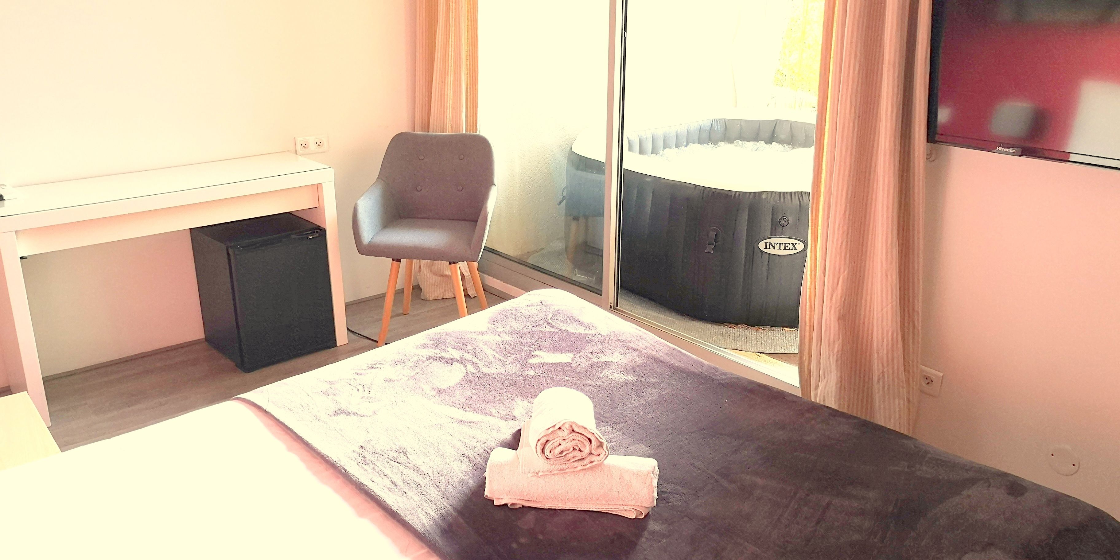 A hotel room with a bed, a chair, a small table, and a hot tub visible through the glass door.