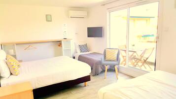 Habitación de hotel con cama, escritorio, una silla y una puerta corrediza de vidrio que da a un área exterior.