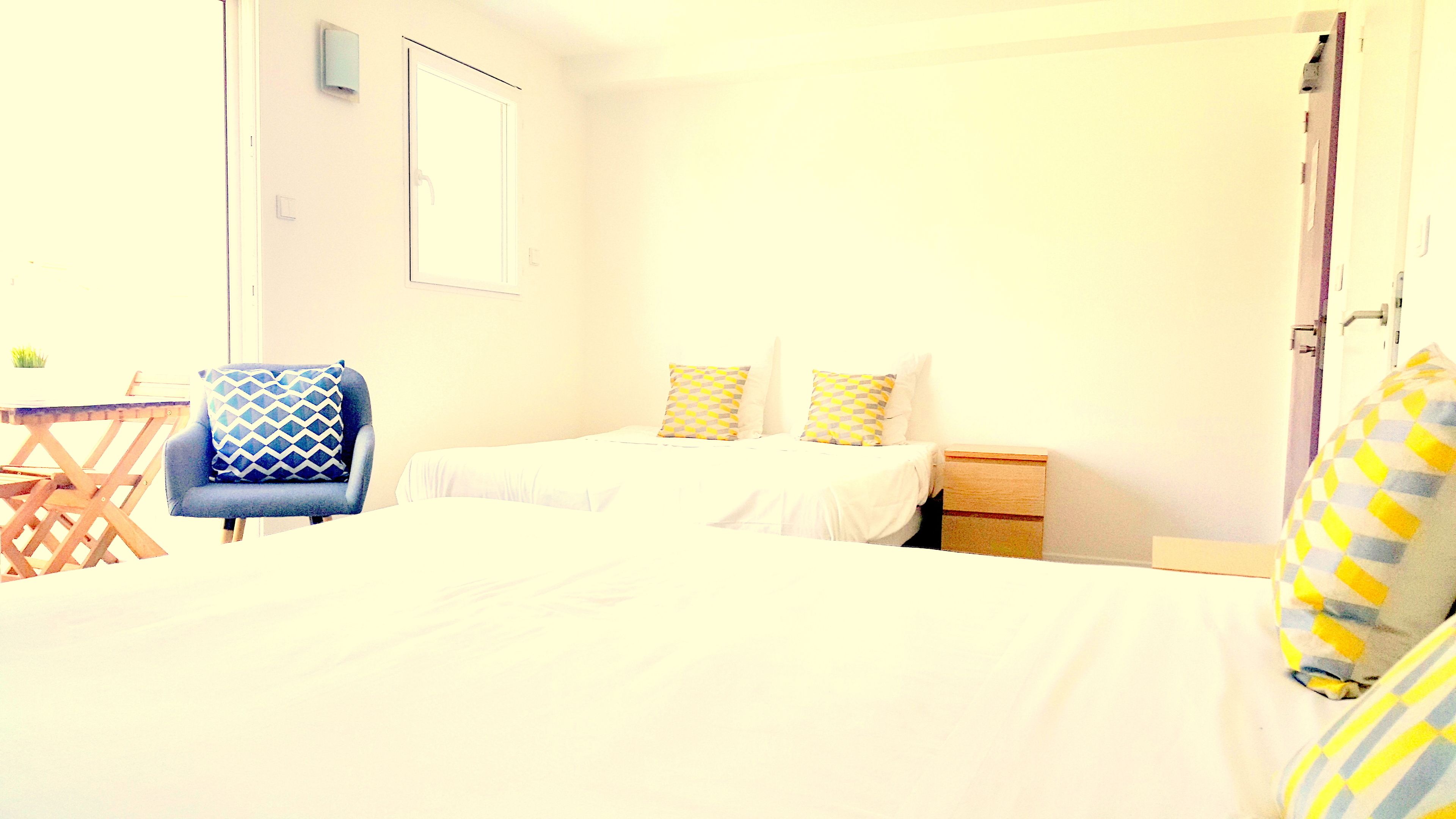 A bedroom with two beds, a chair, a small table, and a nightstand.