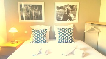 A hotel room with a bed, two patterned pillows, a nightstand with a lamp, and two framed pictures on the wall.