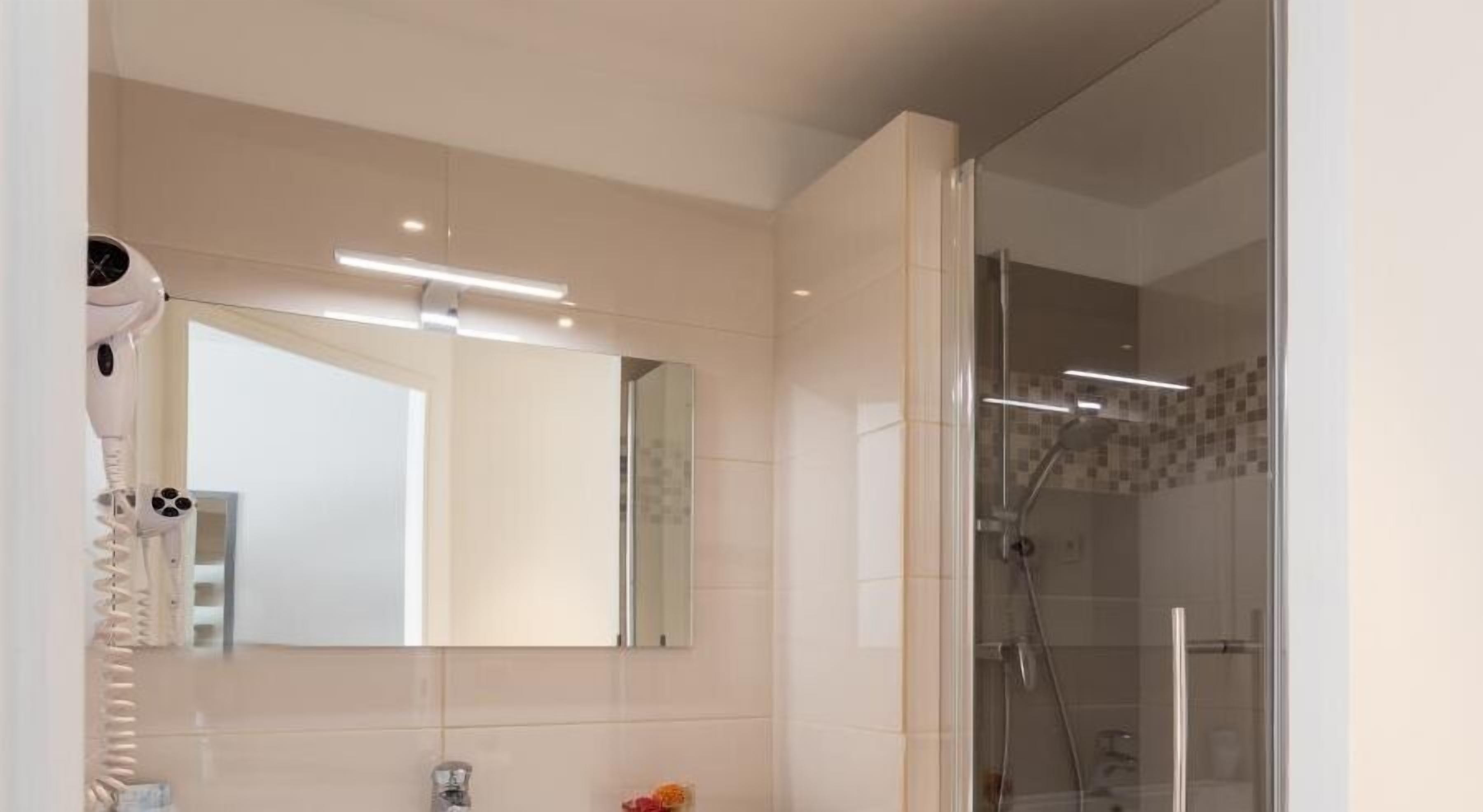 A modern bathroom with a large mirror, a hairdryer, and a glass-enclosed shower.