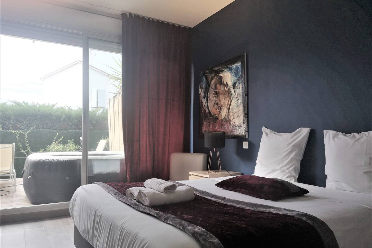 A modern bedroom with a large bed, a view of the outdoors, and a painting on the wall.