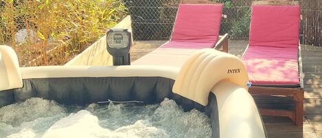 An inflatable hot tub with a control panel, surrounded by a wooden deck and two pink lounge chairs.