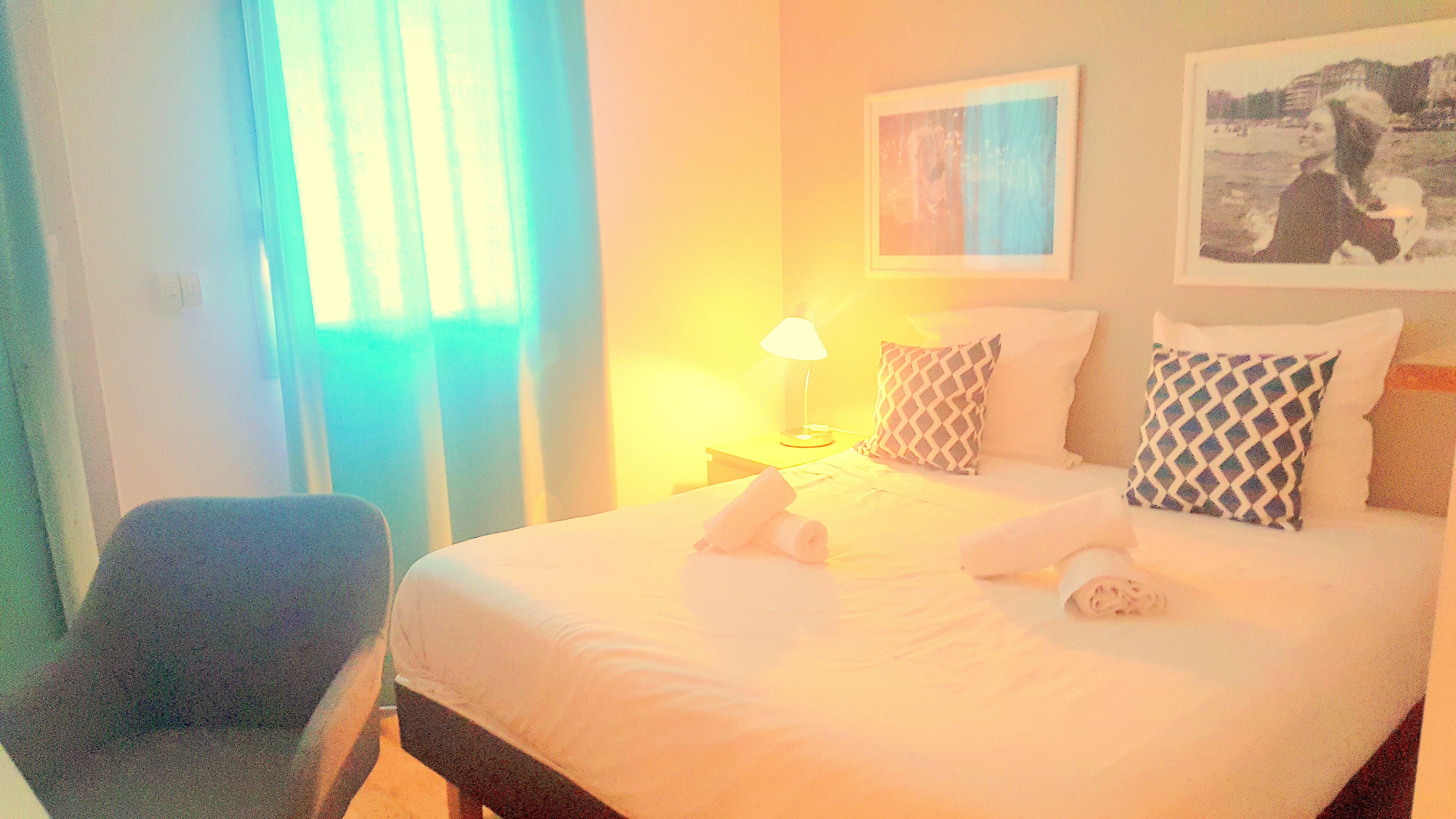 A hotel room with a bed, a chair, a lamp, and a painting on the wall.