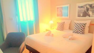 A hotel room with a bed, a chair, a lamp, and a painting on the wall.