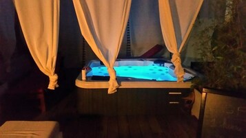 A hot tub with a blue light, surrounded by curtains, and a plant to the right.
