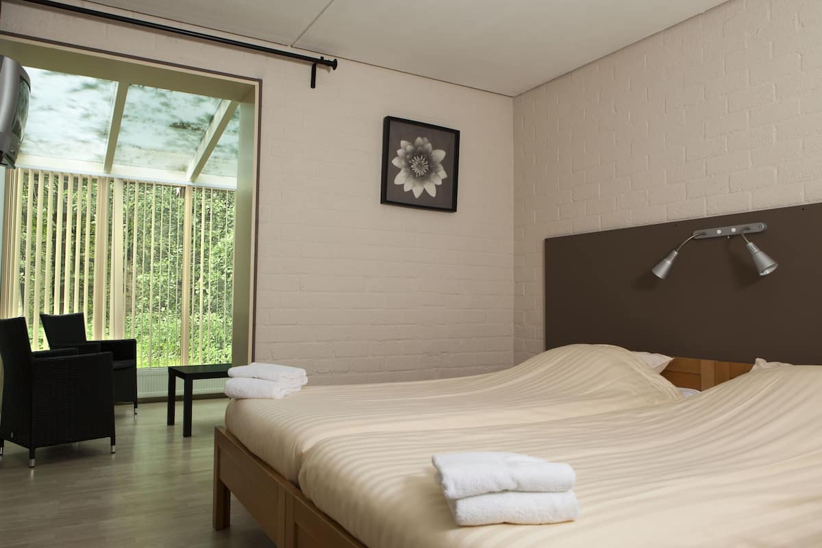 Una habitación de hotel moderna con una cama grande, una mesita, una silla y un ventanal con persianas.