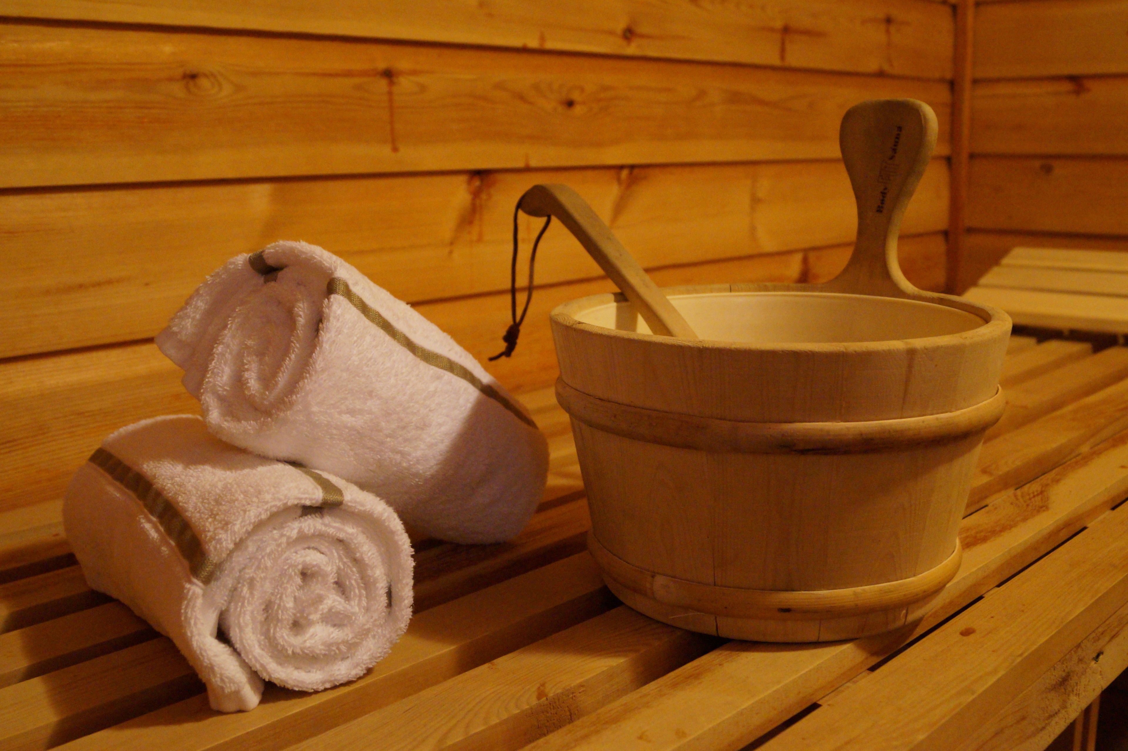 A wooden bench with a wooden bucket and rolled towels.