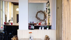 A restaurant with a wooden dining table, chairs, and a bar area with bottles and a wreath. - Hotel de Oorsprong (Sint Nicolaasga)