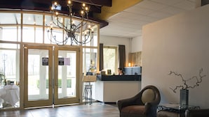 A lobby with a chandelier, a reception desk, and a seating area with a chair and a table. - Hotel de Oorsprong (Sint Nicolaasga)