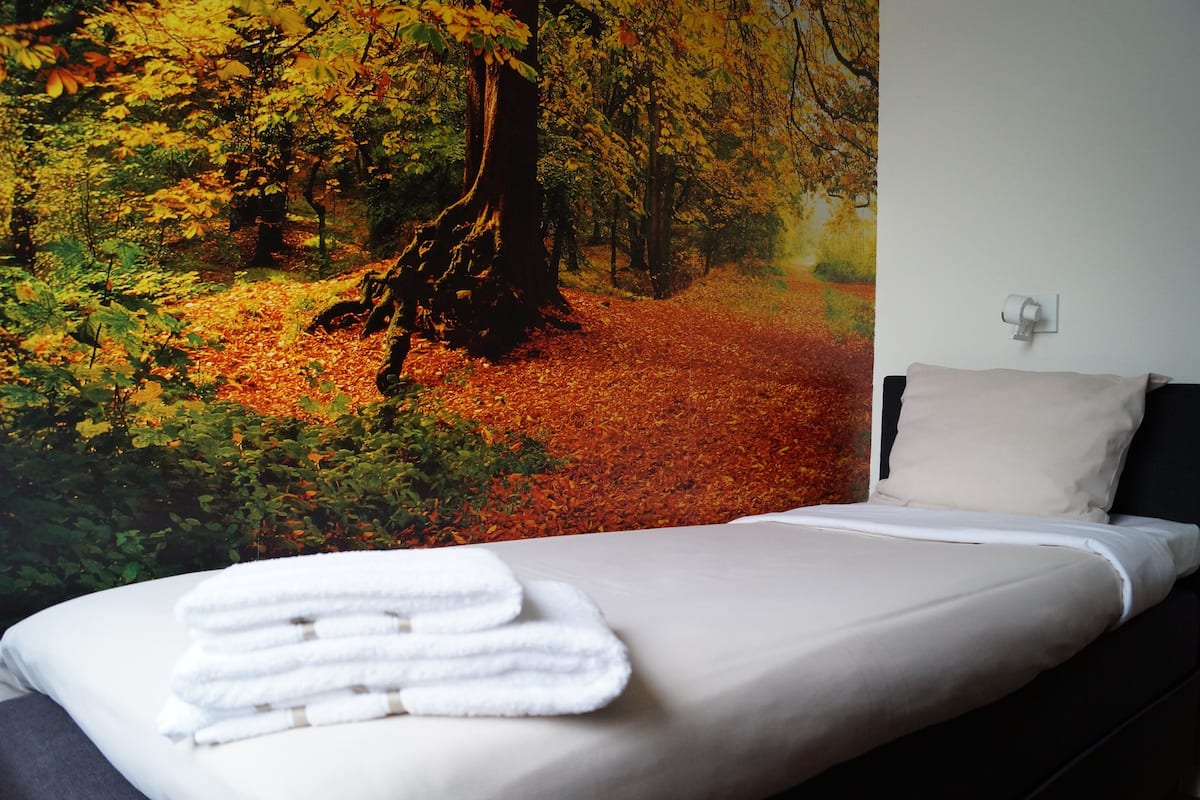 Un dormitorio con cama, almohada y un mural en la pared que muestra un paisaje boscoso.
