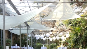 An outdoor dining area with wooden tables and chairs, covered by a transparent roof, and surrounded by greenery. - Hotel de Oorsprong (Sint Nicolaasga)