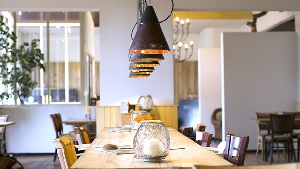 A dining area with a long wooden table, chairs, and a hanging pendant light. - Hotel de Oorsprong (Sint Nicolaasga)