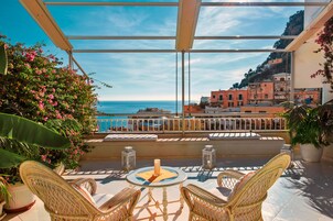Un balcón con sillas de mimbre, una mesa con vela y vistas al mar y edificios.