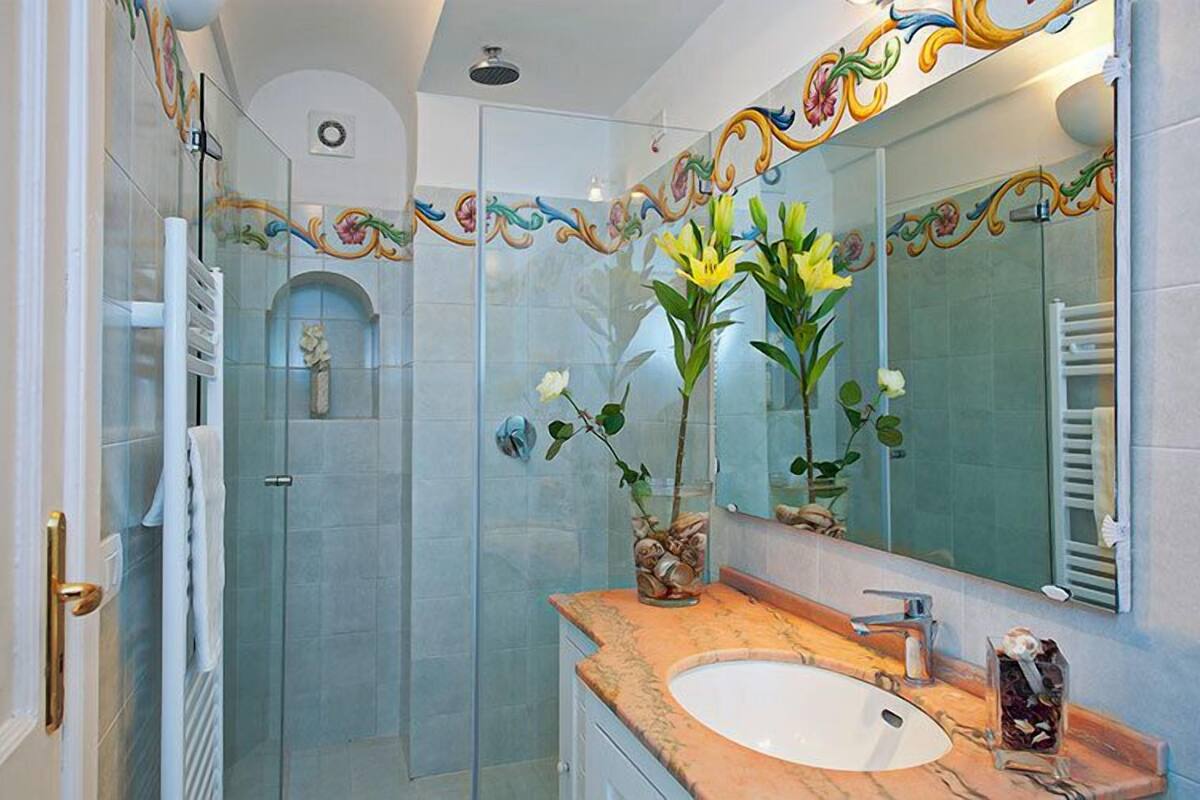 A bathroom with a glass shower enclosure, a white sink, and a mirror with decorative tiles.
