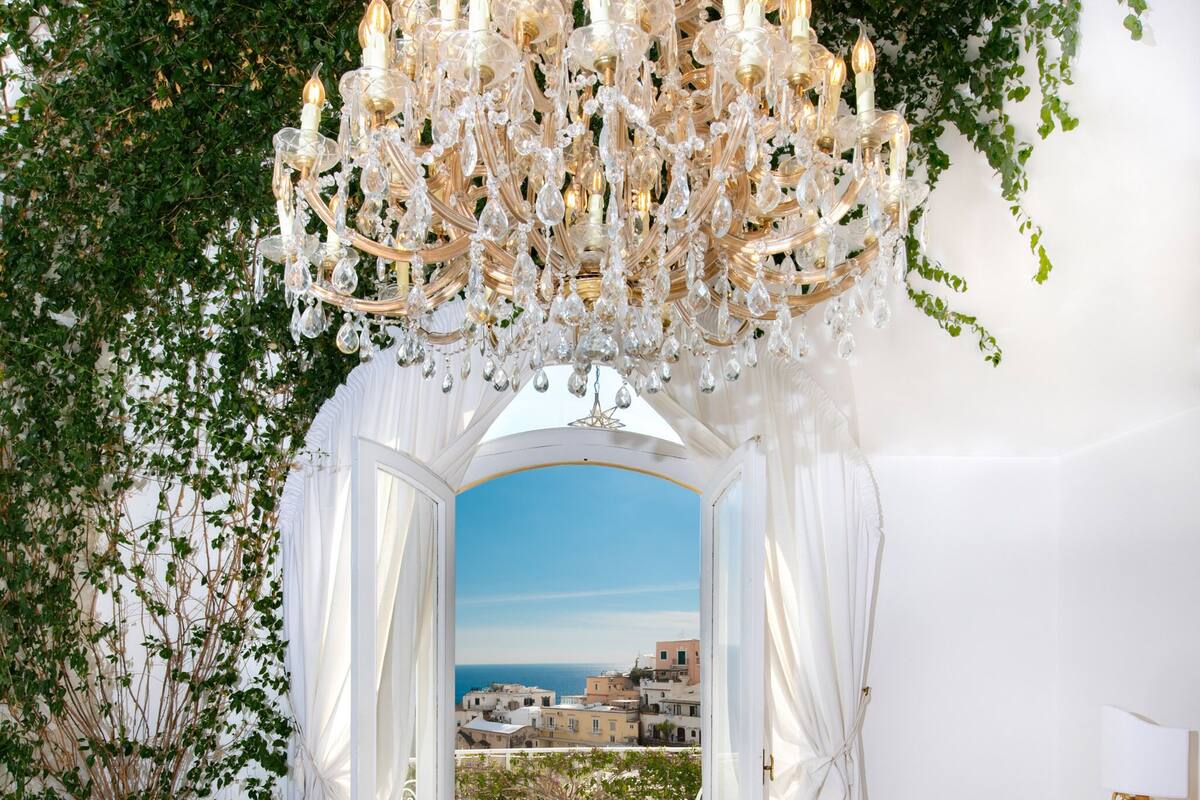 A luxurious bedroom with a large bed, a chandelier, and a view of the sea.