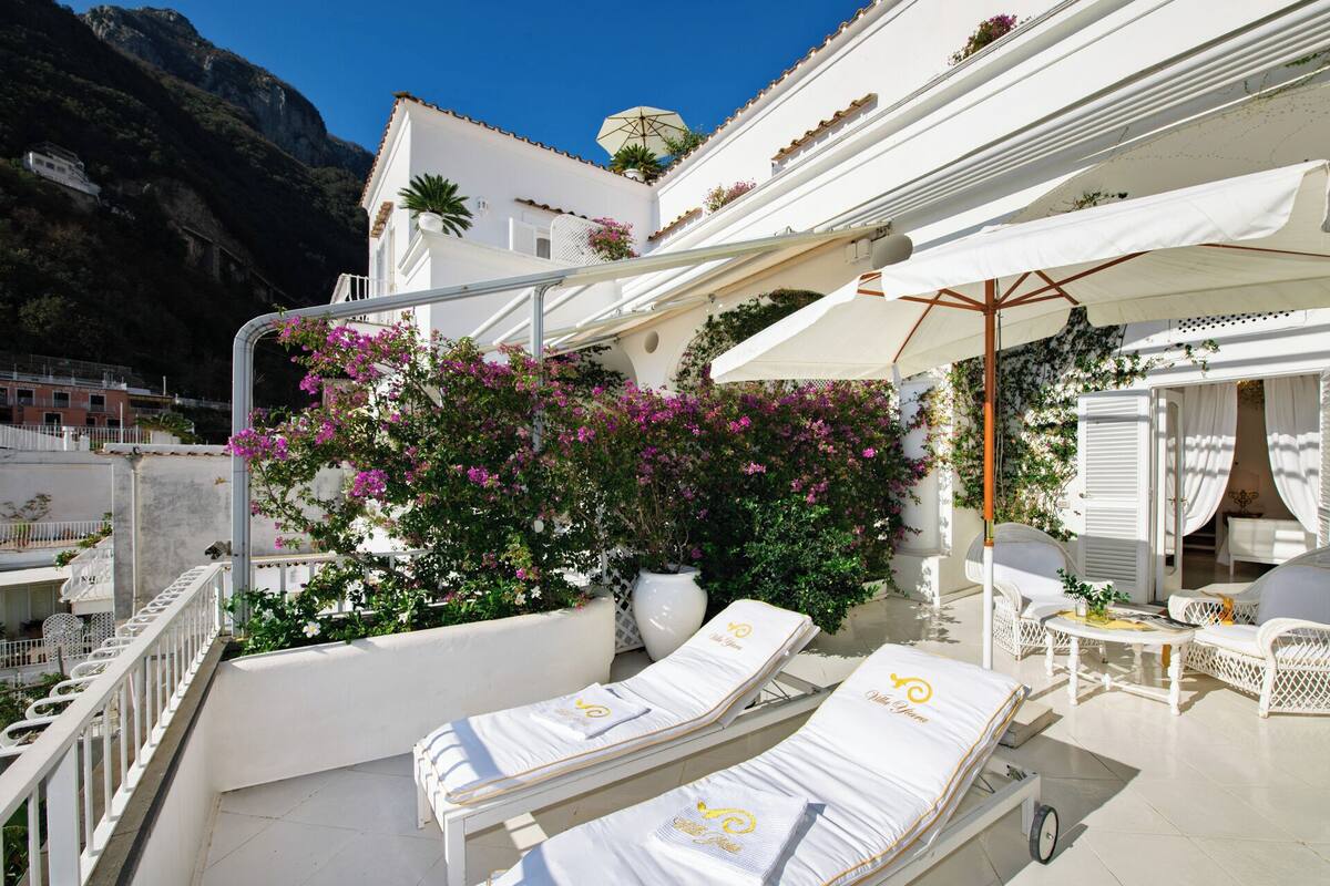 A hotel balcony with white lounge chairs, a potted plant, and a view of a mountain.