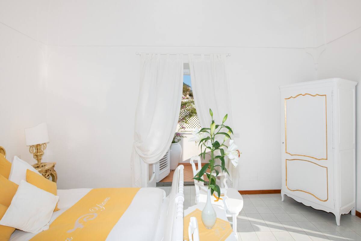 A bedroom with a bed, a nightstand, a white wardrobe, and a view of the outdoors.