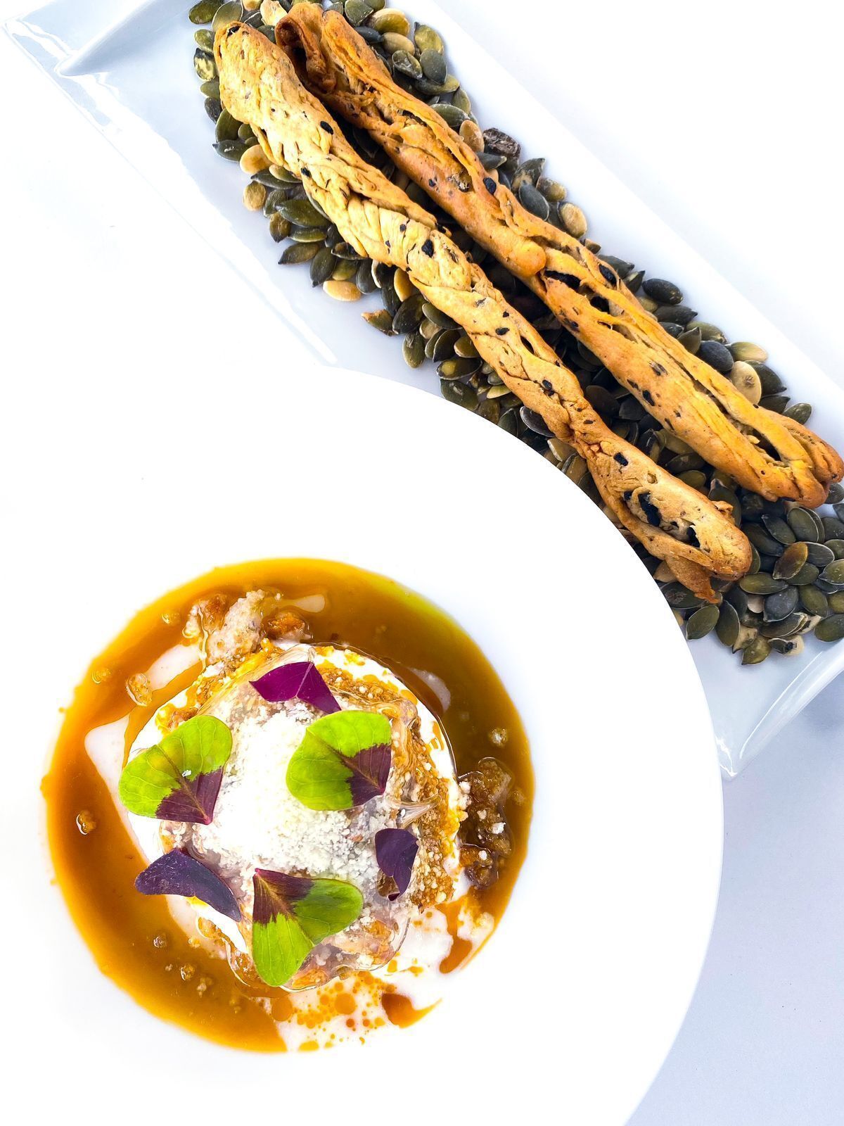 Un plato de postre con una base cremosa, decorado con hojas moradas y una salsa.