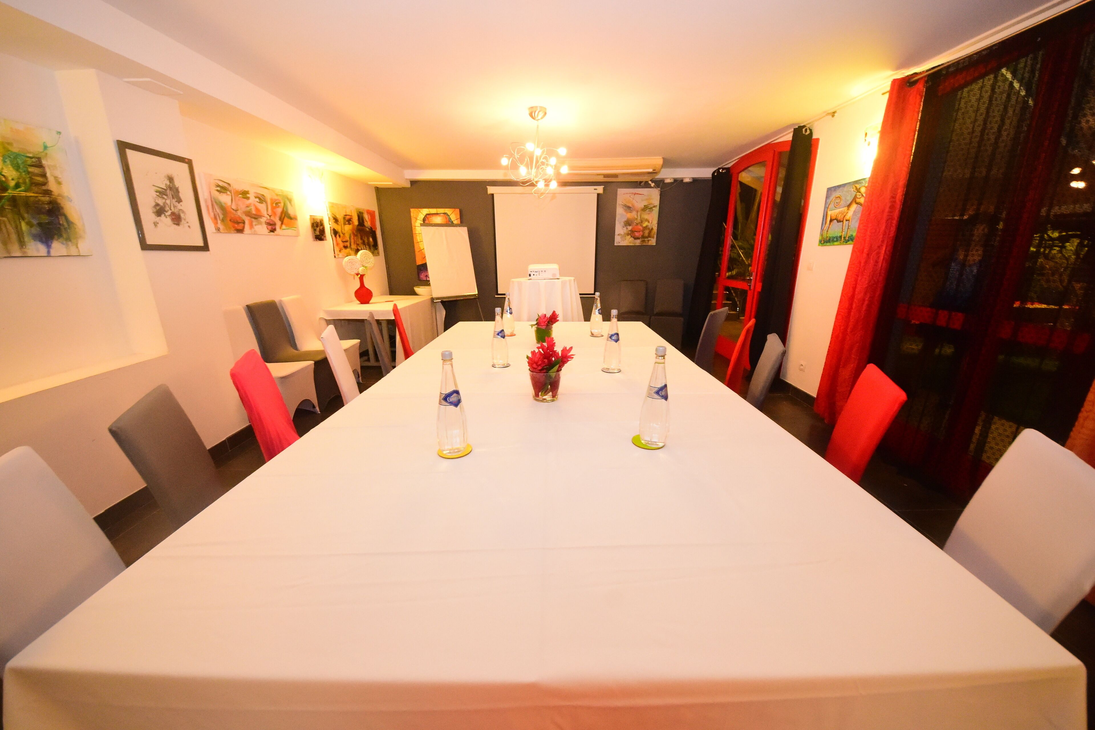 A conference room with a long table, white chairs, and a projector screen.