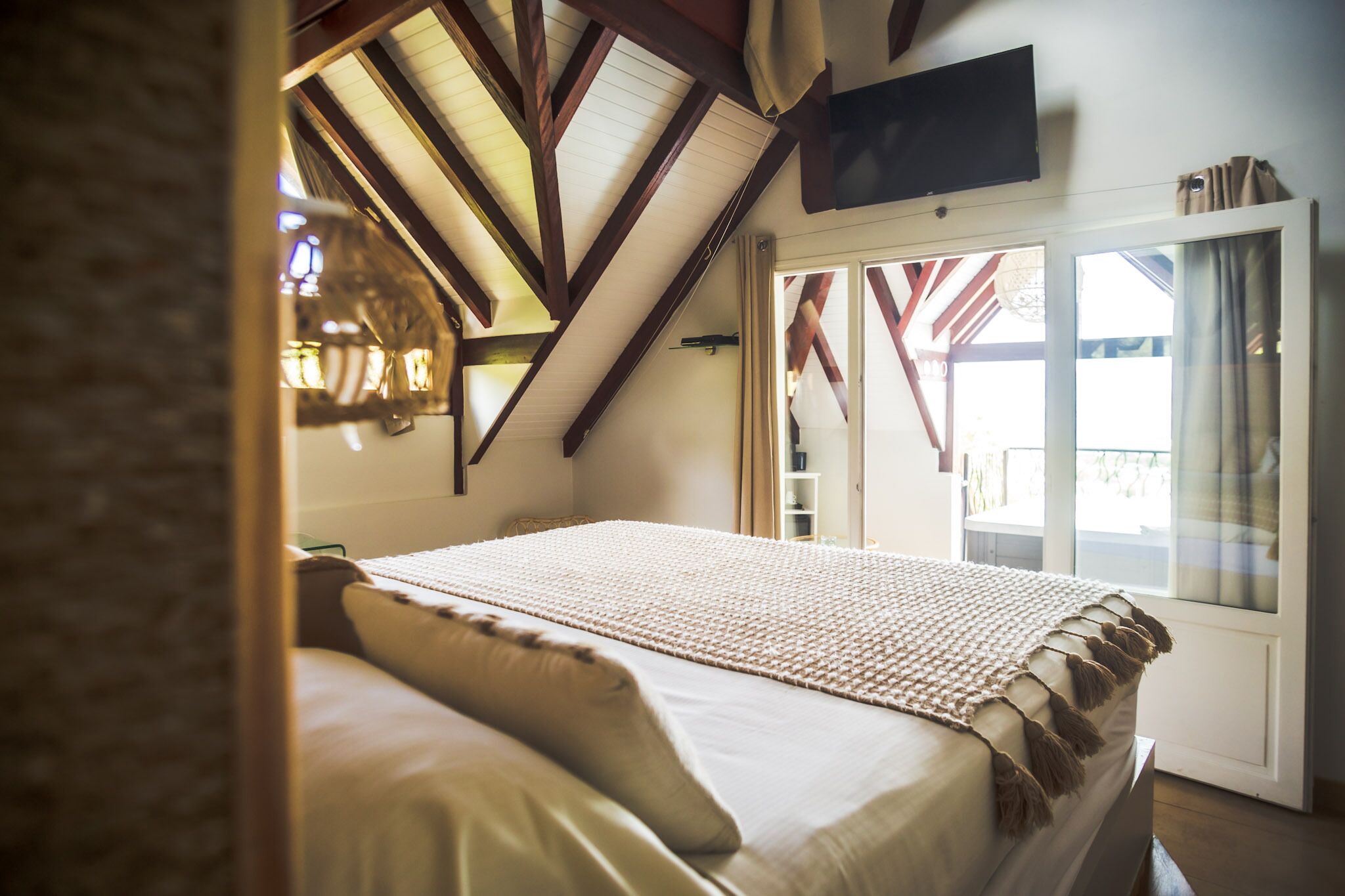 Une chambre avec un grand lit, un téléviseur fixé au mur et une fenêtre avec des rideaux.