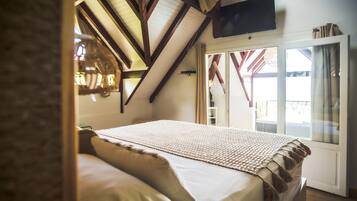 A bedroom with a large bed, a TV mounted on the wall, and a window with curtains.