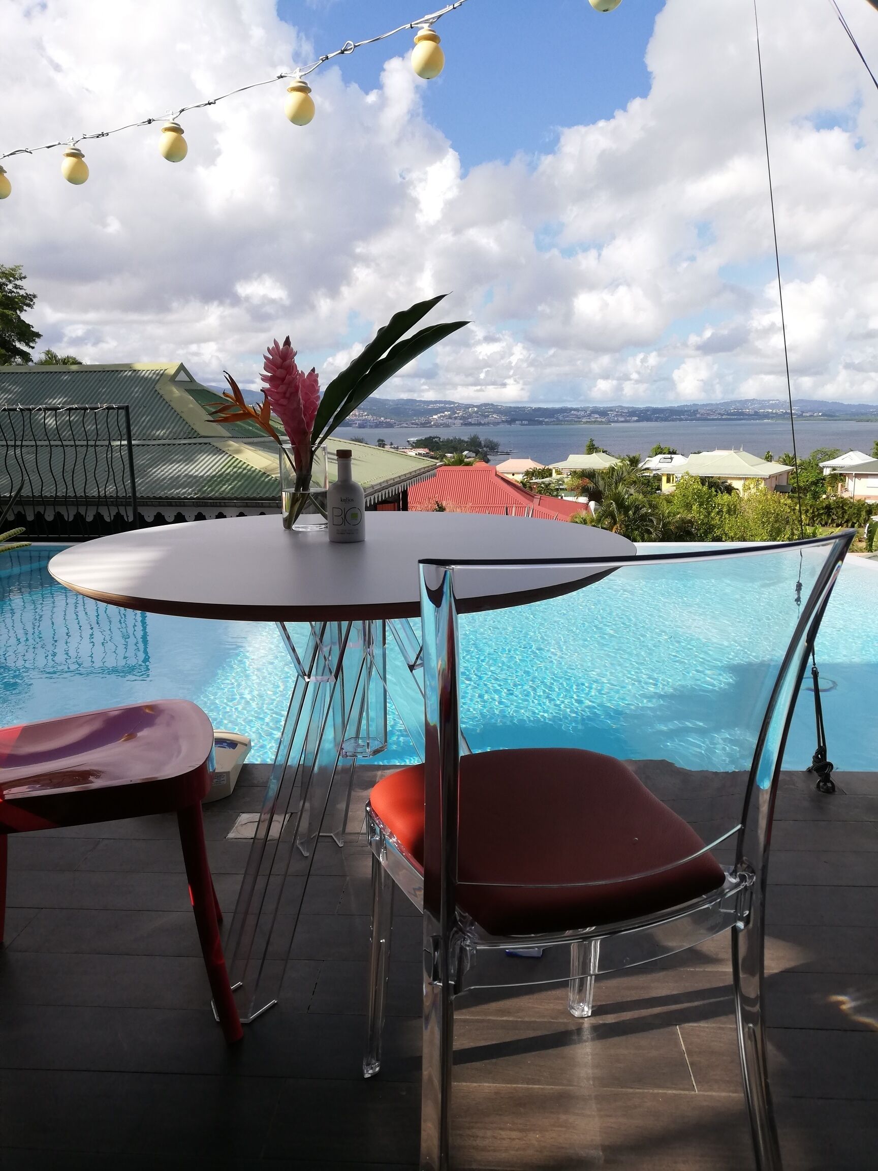 Un área junto a la piscina con una mesa y sillas, una botella de loción y vistas a un paisaje costero.
