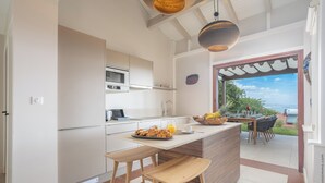 A modern kitchen with a central island, bar stools, and a view of the outdoors. - La Suite Villa (Trois-Ilets)